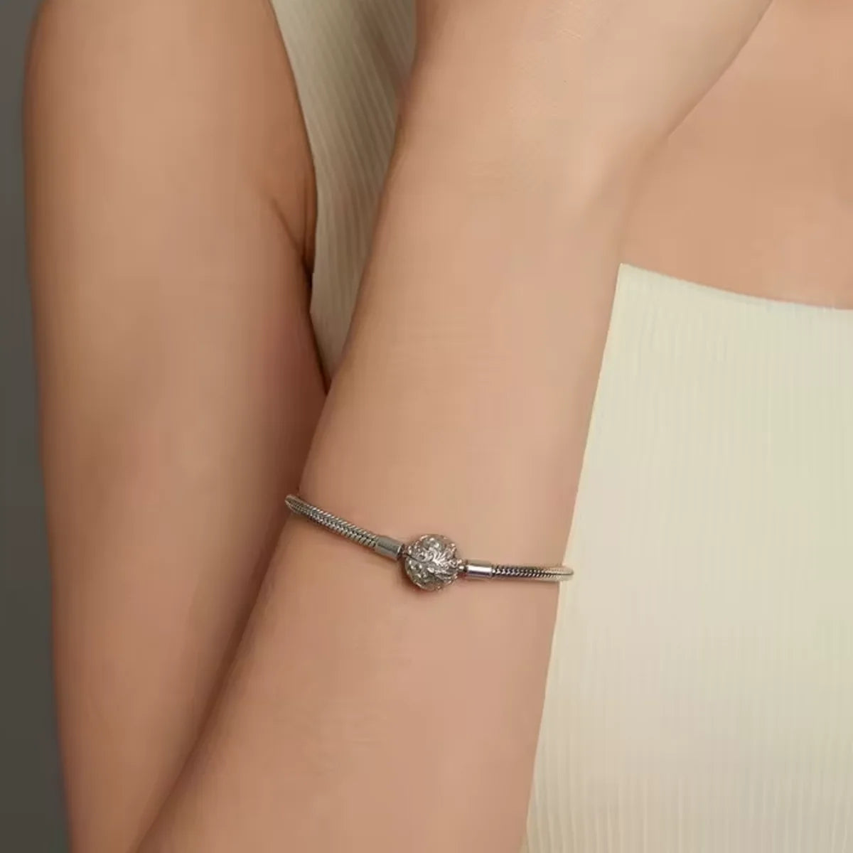 Silver bracelet with a round charm on a person's wrist against a neutral background