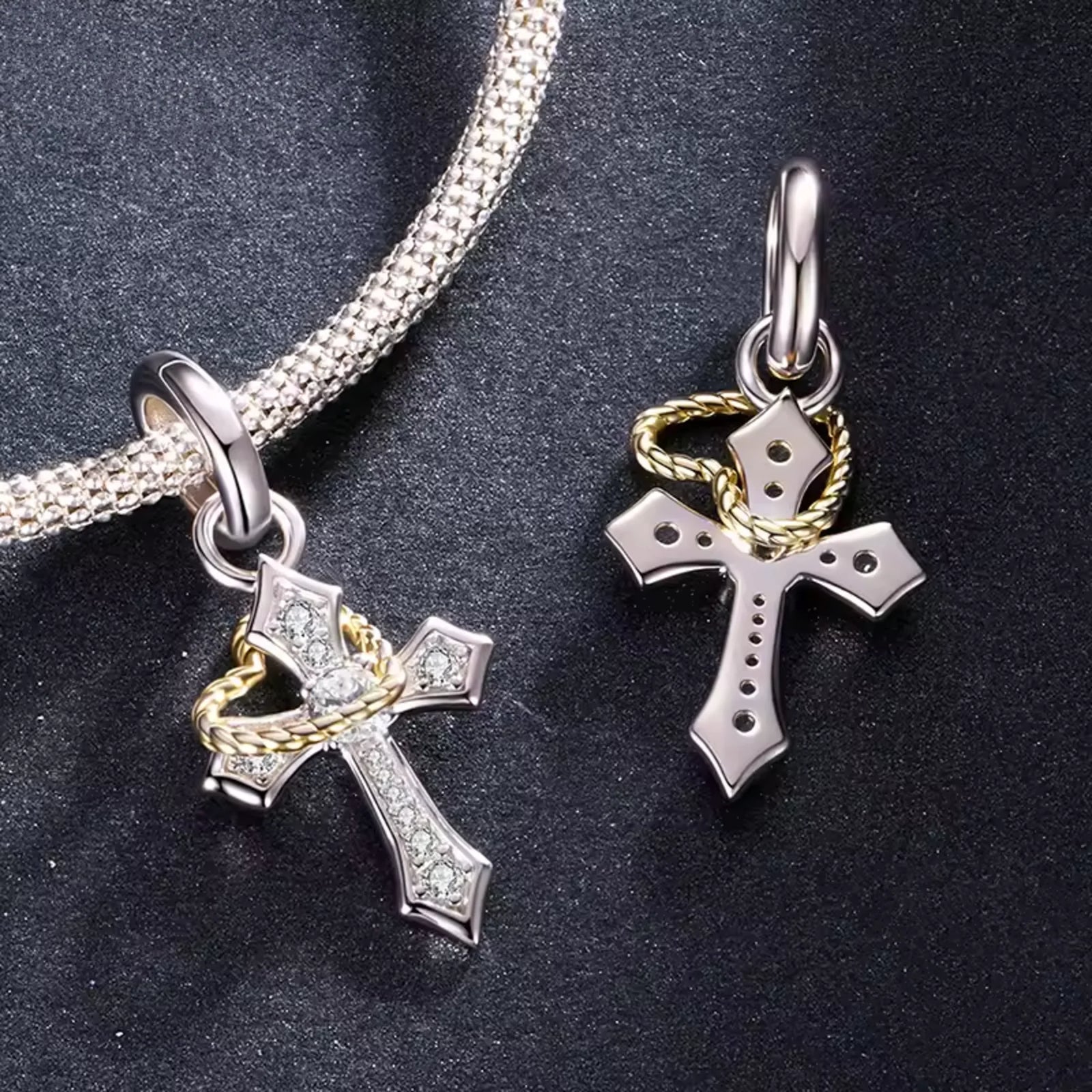 Two silver cross pendants with gold accents on a dark surface