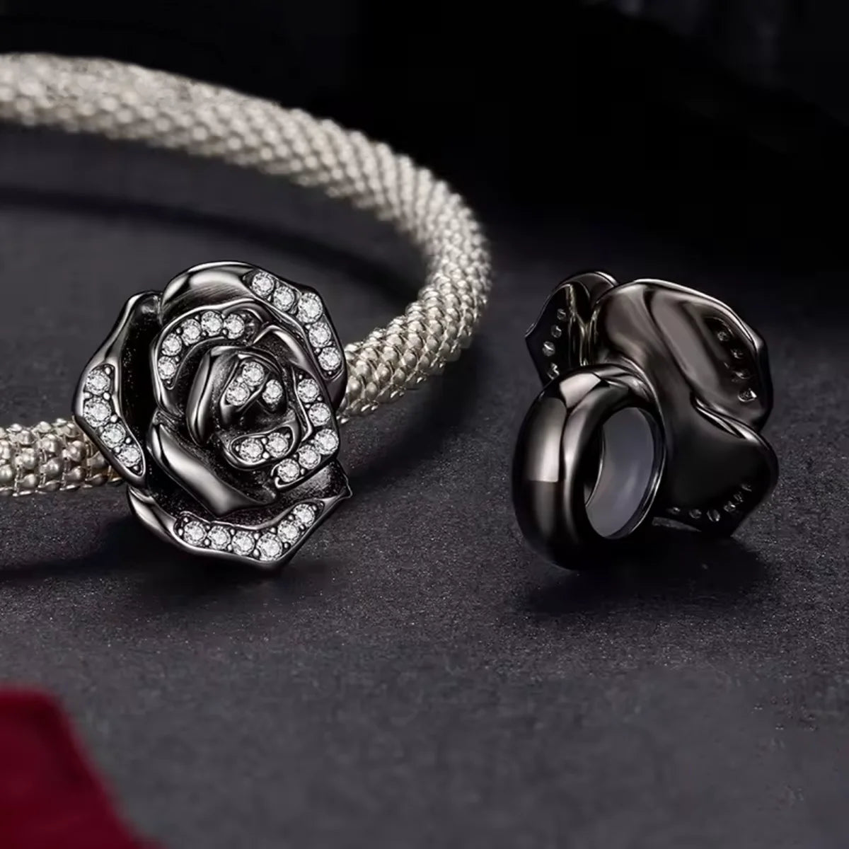 Silver rose-shaped pendant and black circular pendant on a dark surface