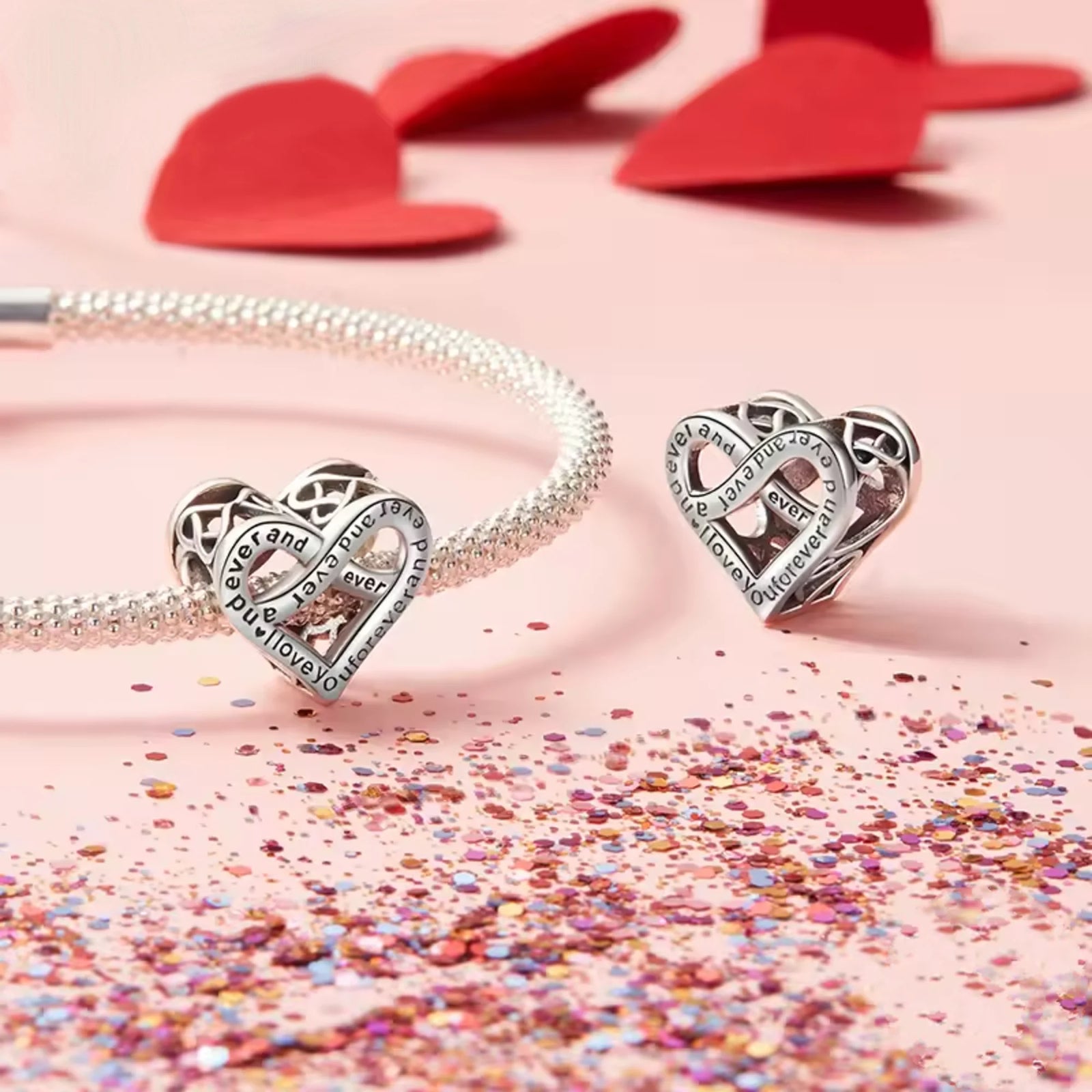 Heart-shaped silver charms on a pink background with confetti