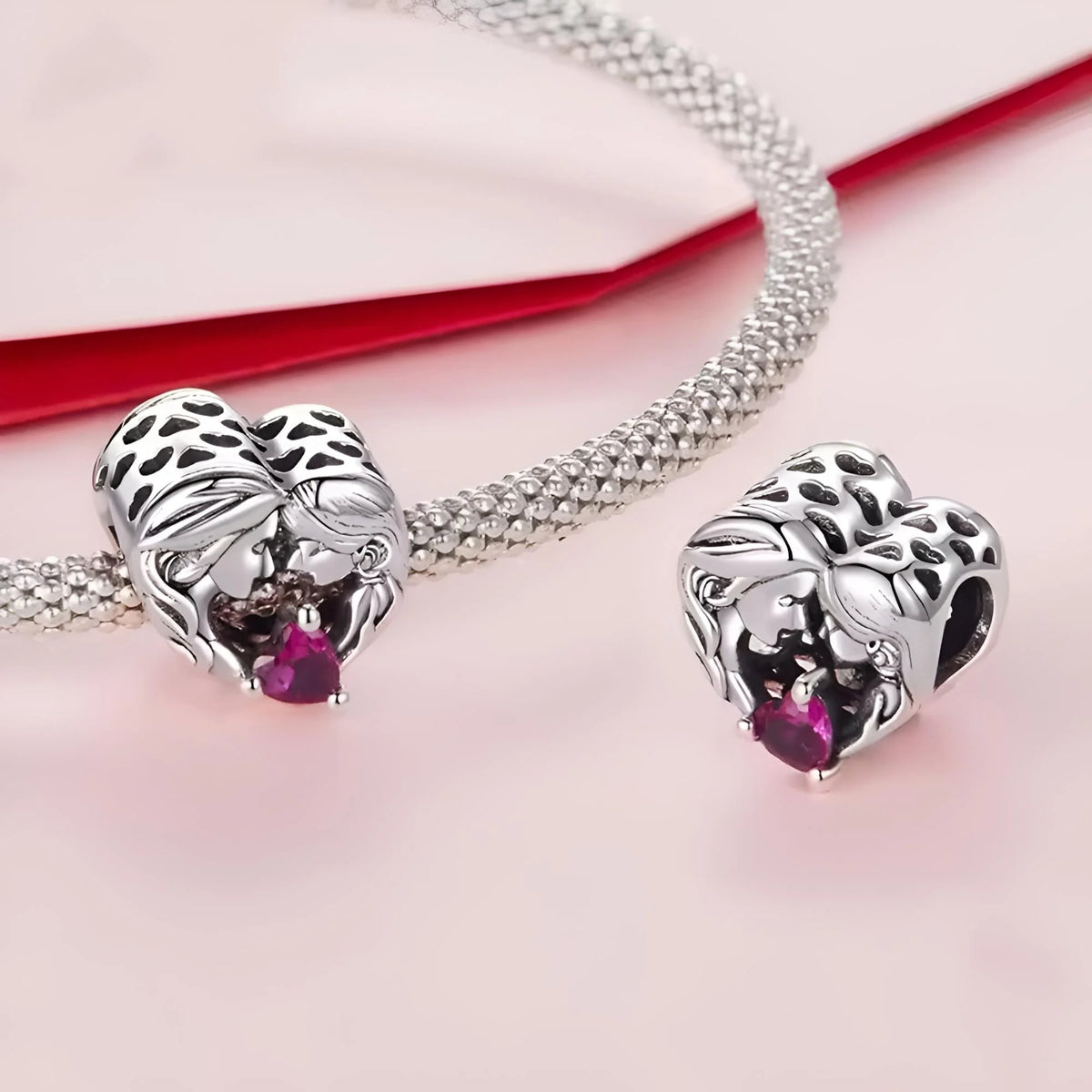 Silver elephant-shaped charms with red gemstones on a pink background