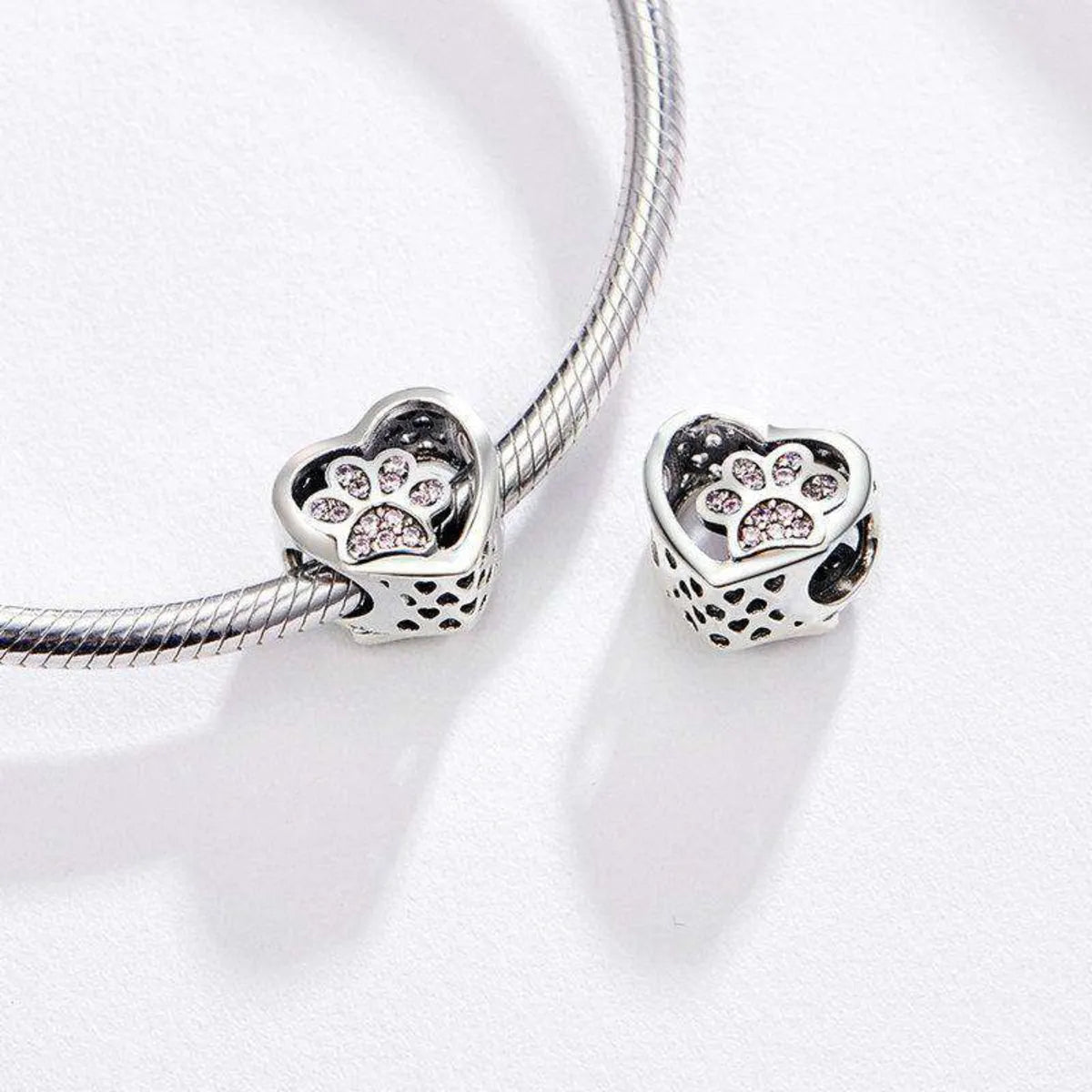Heart-shaped silver charms with paw prints and cubic zirconia on a white background