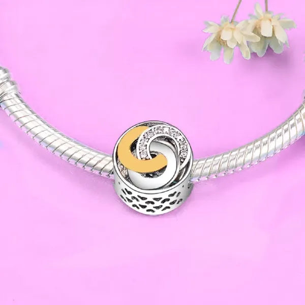 Embrace the beauty of unity and connection with the Trinity Ring Charm. This exquisite design features interlocking circles, symbolizing eternal love and the bond between past, present, and future. Adorned with shimmering cubic zirconia accents and highlighted by a luxurious gold-plated crescent, this charm brings a timeless elegance to your jewellery collection. The sterling silver base, detailed with delicate cut out hearts, ensures it shines brightly on any Pandora-compatible bracelet. Whether you&#39;re cel