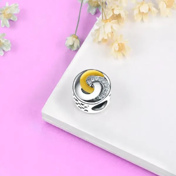 Embrace the beauty of unity and connection with the Trinity Ring Charm. This exquisite design features interlocking circles, symbolizing eternal love and the bond between past, present, and future. Adorned with shimmering cubic zirconia accents and highlighted by a luxurious gold-plated crescent, this charm brings a timeless elegance to your jewellery collection. The sterling silver base, detailed with delicate cut out hearts, ensures it shines brightly on any Pandora-compatible bracelet. Whether you&#39;re cel