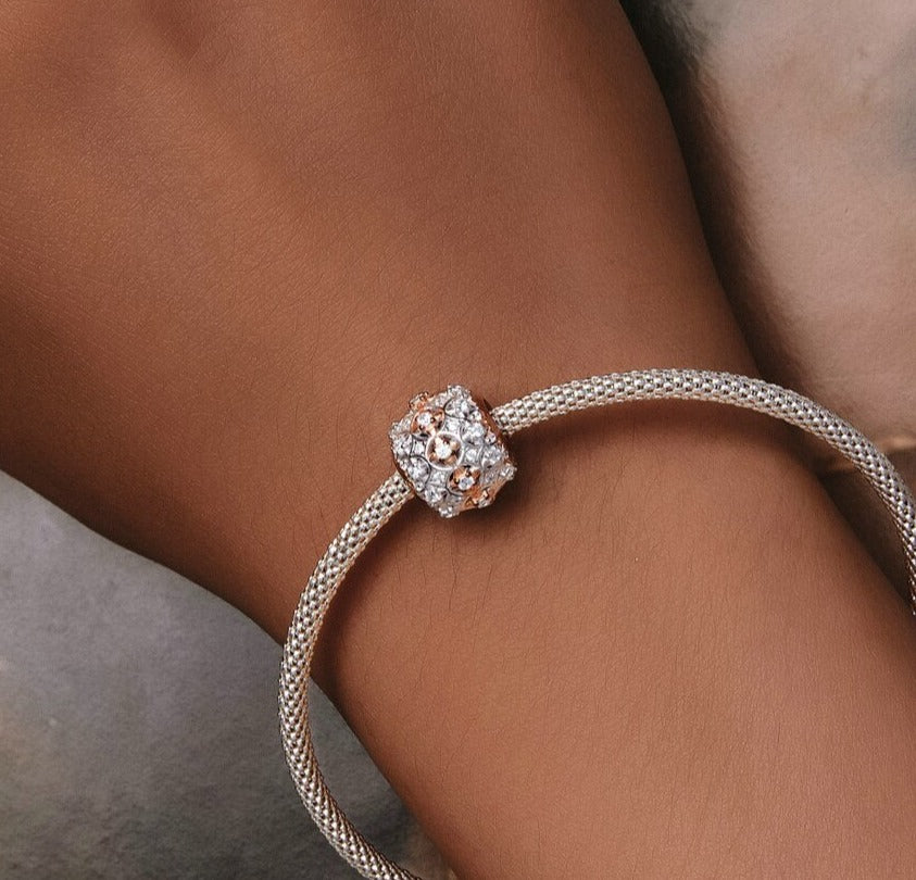 Two-tone round charm with cubic zirconia on a bracelet, featuring sterling silver and rose gold plating, displayed on a wrist.