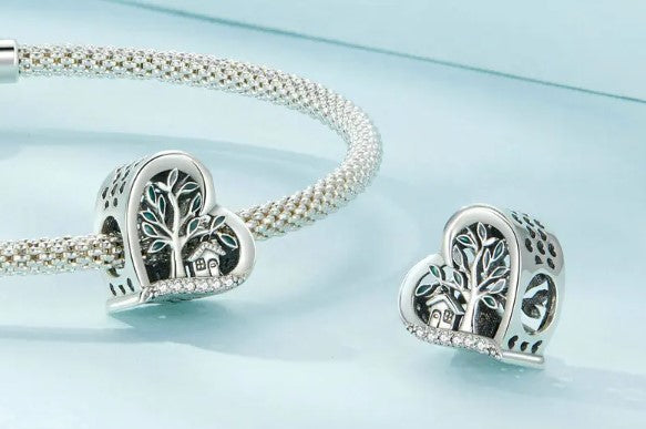 Heart-shaped charm with tree and house design on silver bracelet representing 'Home Is Where The Heart Is' theme.