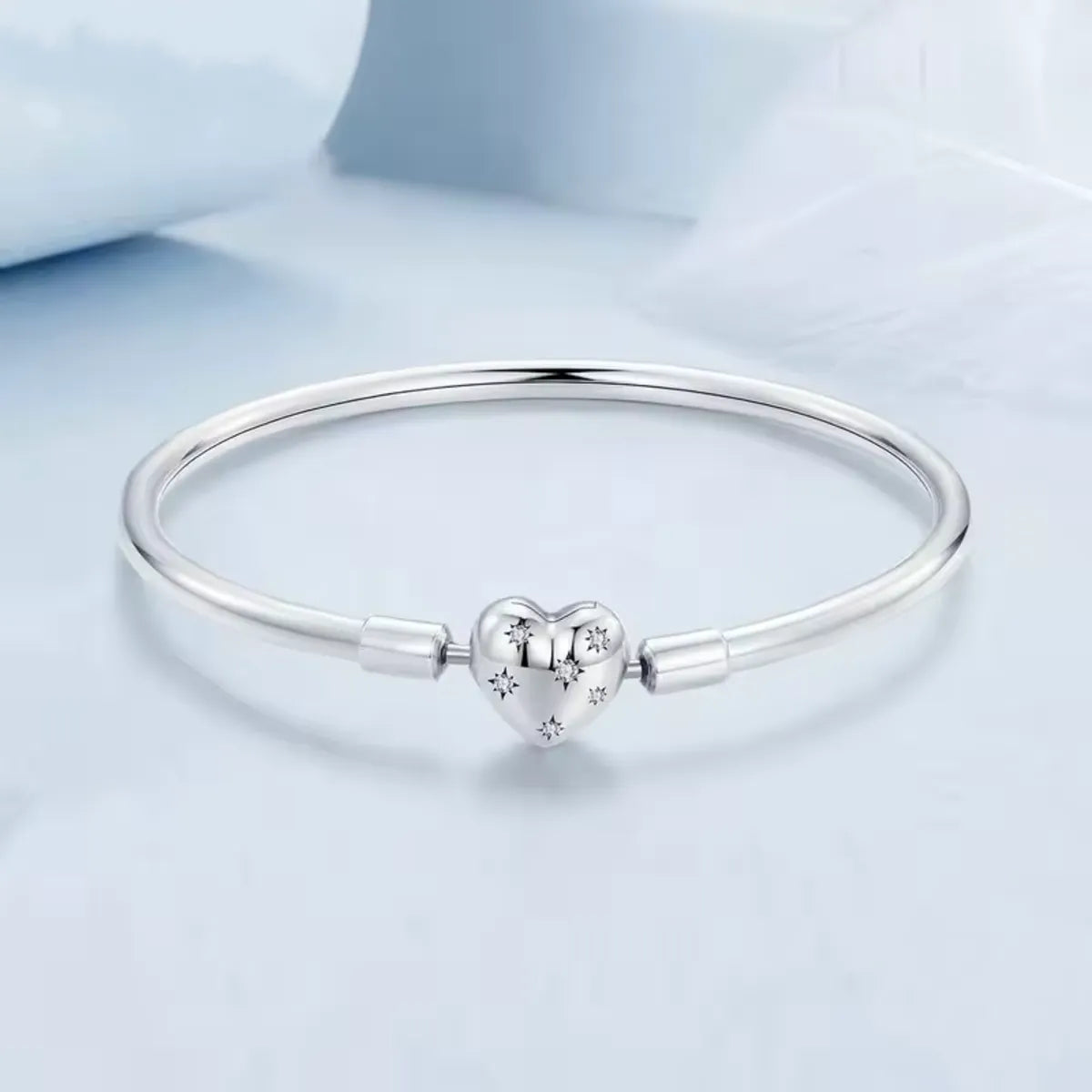 Silver bracelet with a heart-shaped charm on a light blue background