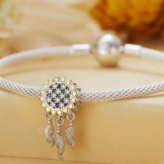 Brighten up your collection with the enchanting Sunflower Dreamcatcher Dangle Charm! This exquisite piece features a beautifully detailed sunflower design, symbolizing happiness and positivity. Adorned with sparkling cubic zirconia and plated in radiant gold.