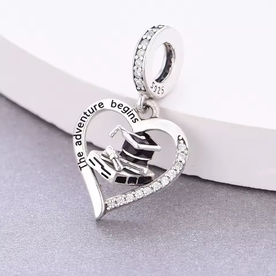Celebrate new beginnings with this stunning Graduation Dangle Charm! Designed in&amp;nbsp;sterling silver, this elegant charm features an open-heart frame engraved with &quot;The Adventure Begins&quot;, surrounding a detailed graduation cap, diploma, and books. The charm is beautifully accented with sparkling Cubic Zirconia stones and black enamel for added contrast and sophistication. Perfect for graduates stepping into their next chapter.
