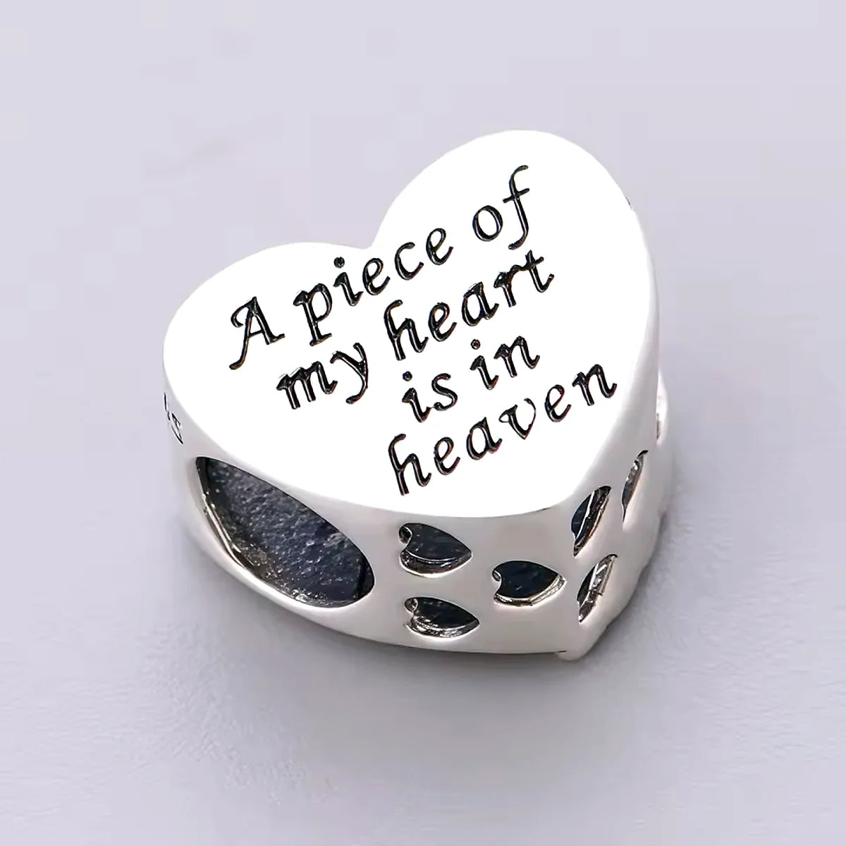 Silver heart-shaped charm with engraved text on a light gray background