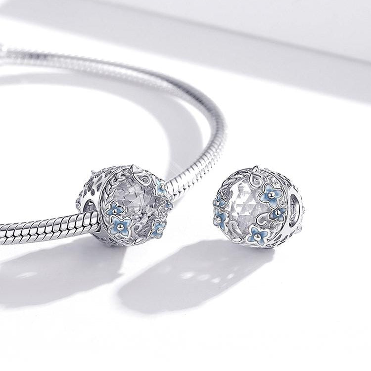 A round sterling silver vintage flower and crystal charm with a white flower and blue cubic zirconia accents.