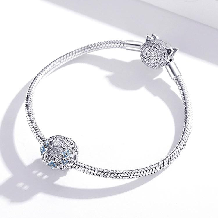 A round sterling silver vintage flower and crystal charm with a white flower and blue cubic zirconia accents.