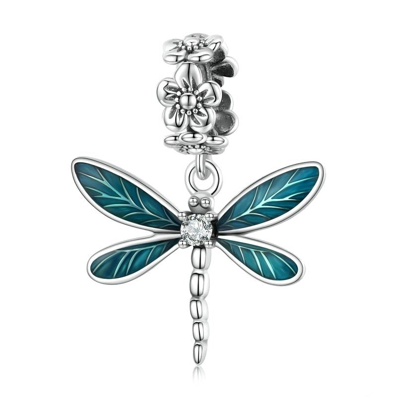 A sterling silver dangle charm in the shape of a dragonfly with floral designs and a blue-colored wing.