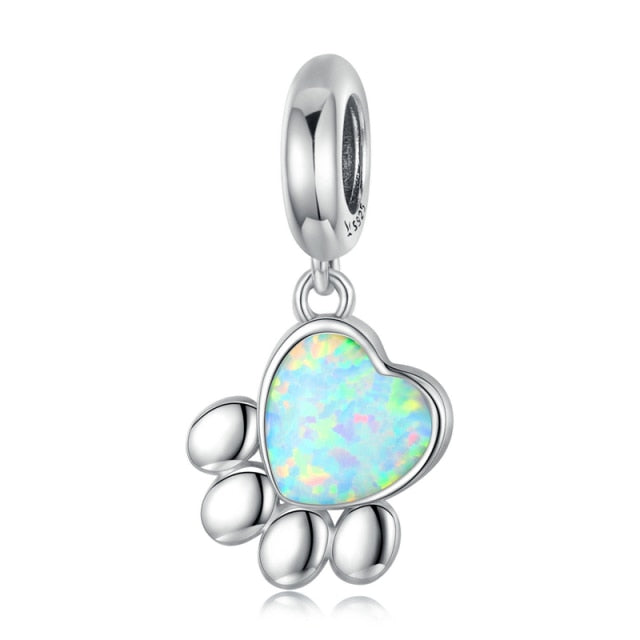 A silver-colored dangle charm featuring a paw print with a blue opal stone in the center, designed for use on bracelets.