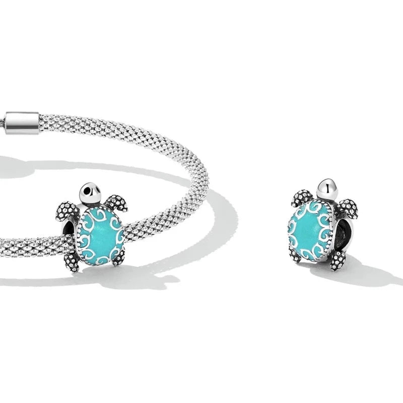 A sterling silver charm in the shape of an underwater turtle with a detailed pattern on its shell and a blue-colored center.